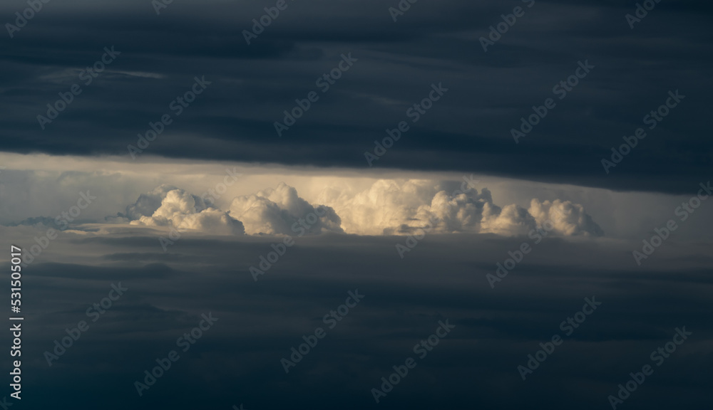Obraz premium Bright sunlit cloud visible through opening in dark cloud, abstract landscape