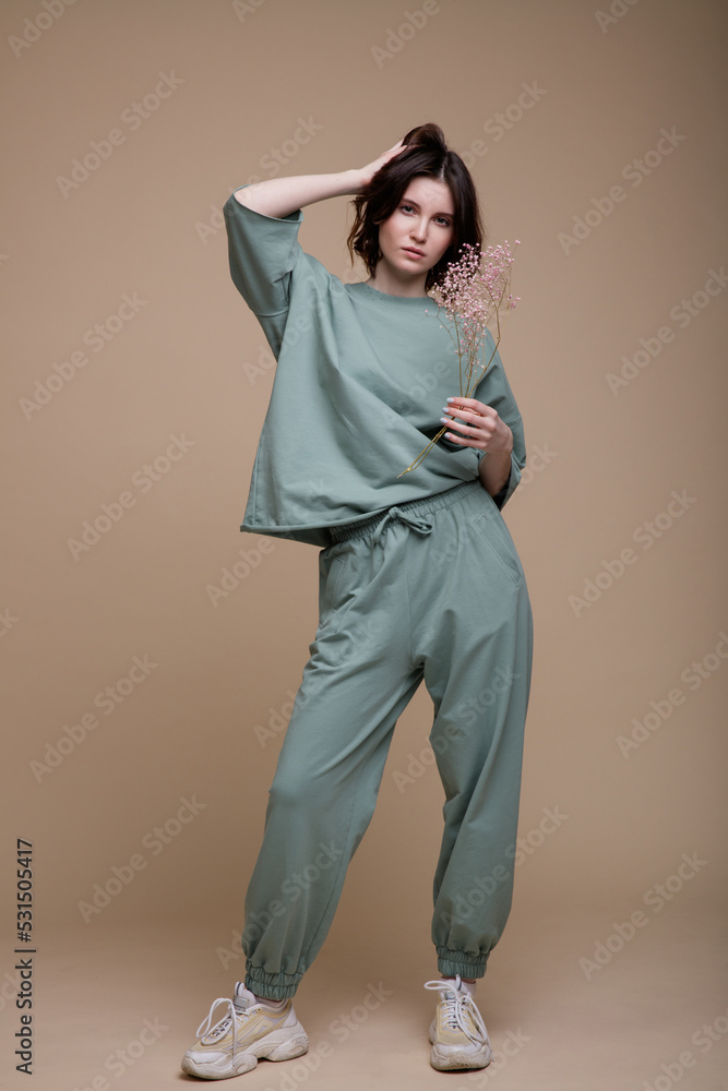 High fashion photo of a beautiful elegant young woman in a pretty green mint sports suit, walking style, oversize posing over brown background. Studio Shot. Portrait. Branch of dried flowers in hands High fashion photo of a beautiful elegant young woman in a pretty green mint sports suit, walking style, oversize posing over brown background. Studio Shot. Portrait. Branch of dried flowers in hands