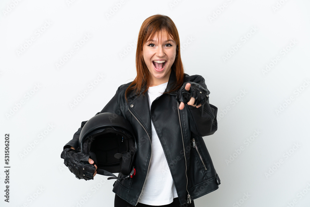 Redhead girl with a motorcycle helmet isolated on white background surprised and pointing front