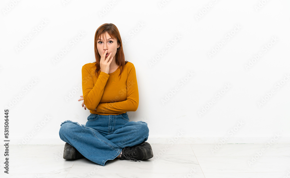 Redhead girl sitting on the floor isolated on white background surprised and shocked while looking right Redhead girl sitting on the floor isolated on white background surprised and shocked while looking right