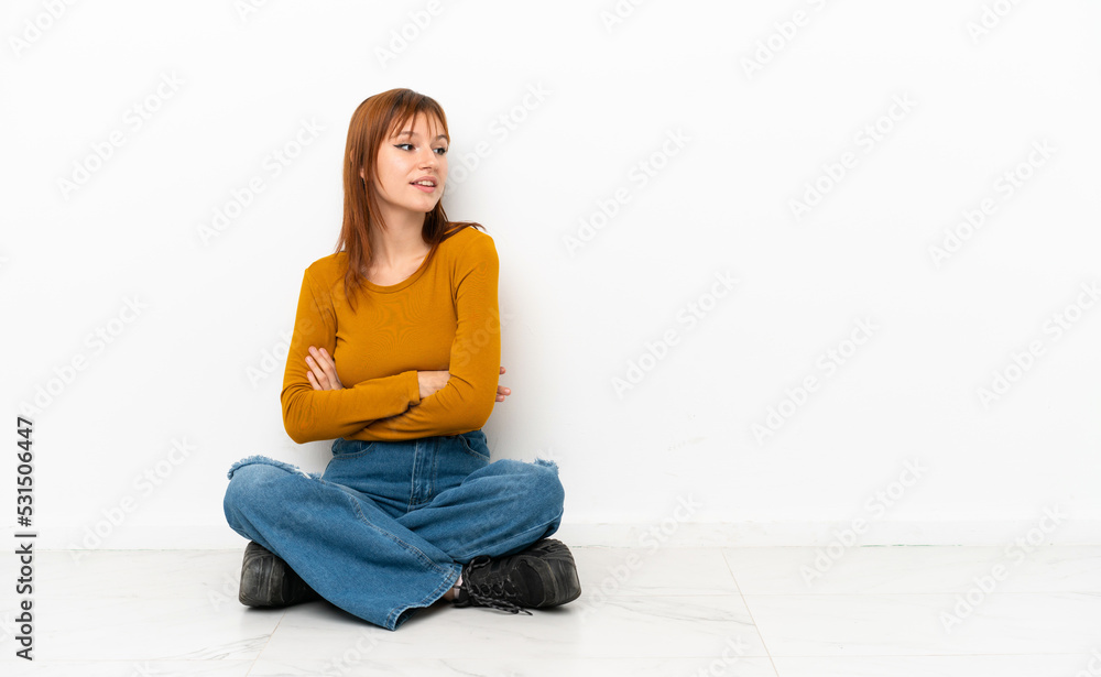 Redhead girl sitting on the floor isolated on white background with arms crossed and happy Redhead girl sitting on the floor isolated on white background with arms crossed and happy