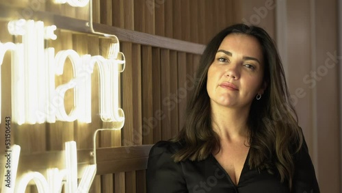 Mujer joven blanca con la luz amarilla de un neon mira a cámara y posa