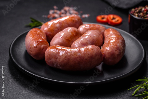 Grilled sausages with spices and herbs on a black background