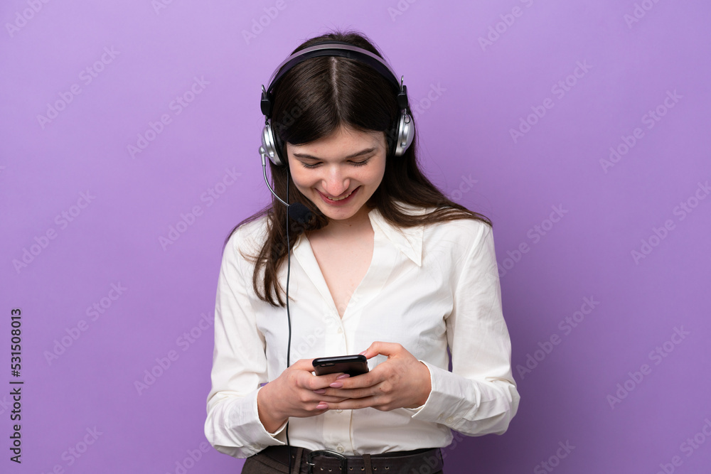Telemarketer Russian woman working with a headset isolated on purple background sending a message with the mobile Telemarketer Russian woman working with a headset isolated on purple background sending a message with the mobile