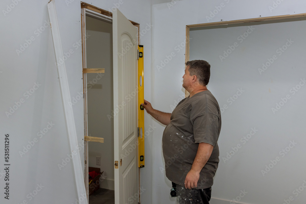 Worker levels the interior doors in a new house as they are being installed, checks that door is being installed correctly Worker levels the interior doors in a new house as they are being installed, checks that door is being installed correctly