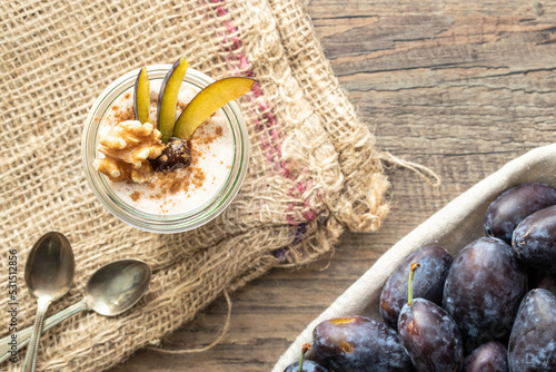 Dessert mit Pflaume, Walnuss, Frischkäse, Joghurt. Quark, Haferflocken, Marmelade und Zimt auf einem Tisch angerichtet photo