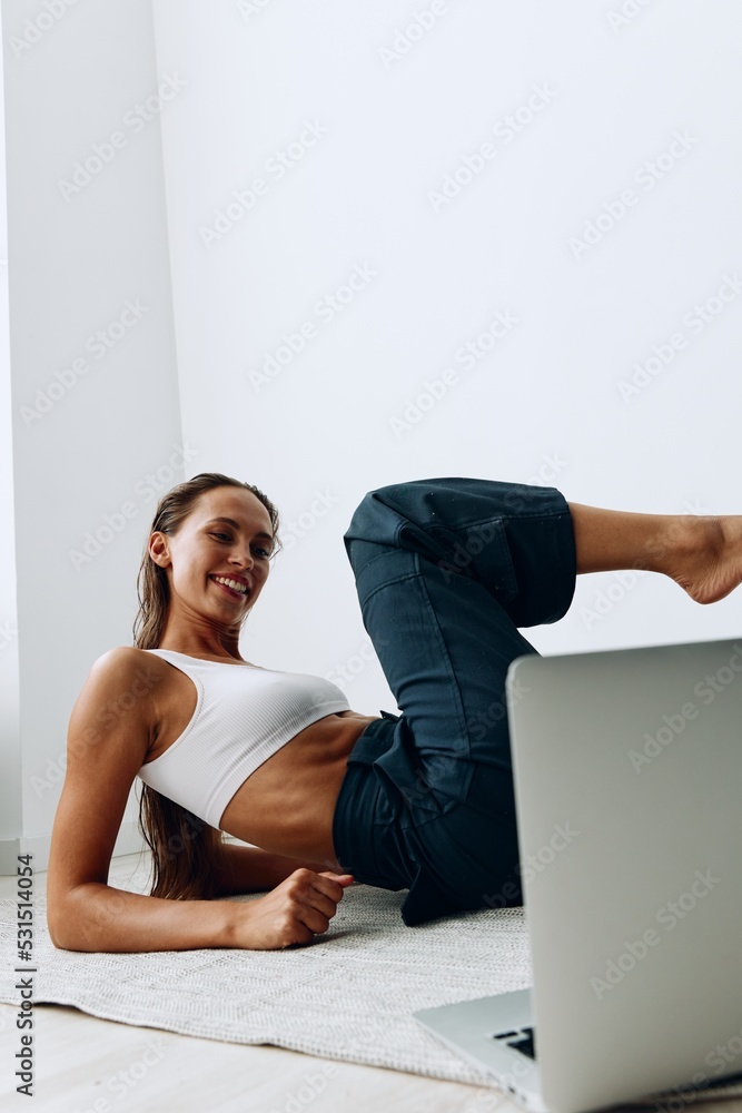 Fototapeta premium A woman goes in for sports on the floor with an online trainer through a laptop. Sports in lockdown