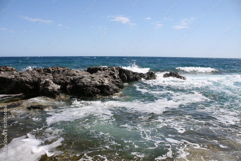 Waves crash over a rock in an aqua blue ocean with a blue sky on top. Image has copy space. Waves crash over a rock in an aqua blue ocean with a blue sky on top. Image has copy space.