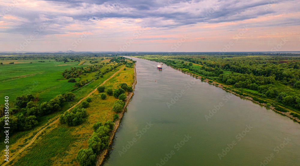 Fototapeta premium Aerial photography of a cargo transport ship seen on Danube at sunrise. Photo was taken from a drone at a higher altitude with camera lowered to keep the ship in focus.