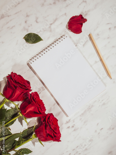 Greeting card for holiday text. Red roses on marble background, white blank sheet. Top view, flatlay
