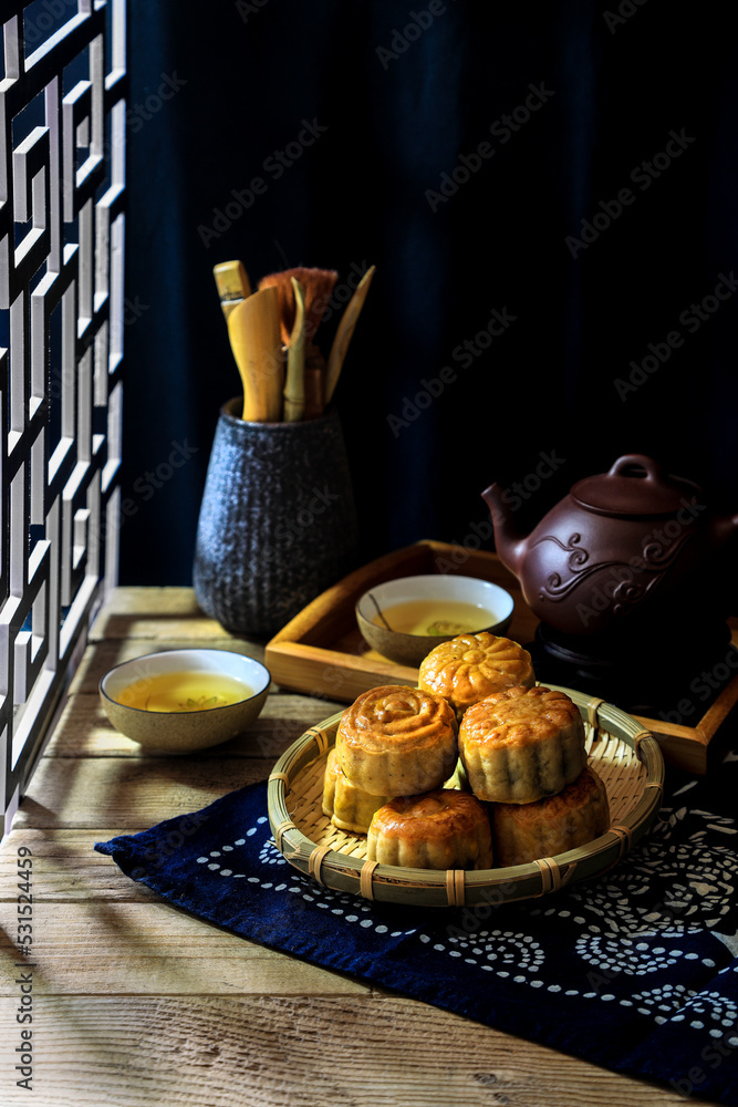 Homemade moon cakes on table and tea pot and cup set at the dark background with light shed from side window - dark and moody photography