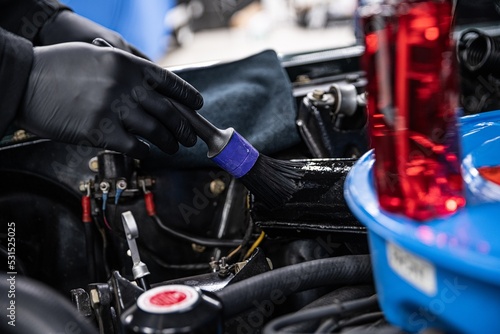 Man worker in a car detailing or car wash studio cleans a car engine with a special brush