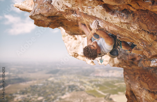 Rock climbing sports and man on mountain cliff for outdoor fitness, wellness goal or workout motivation. Adventure, healthy energy of strong athlete bouldering in safety gear, rope on blue sky nature