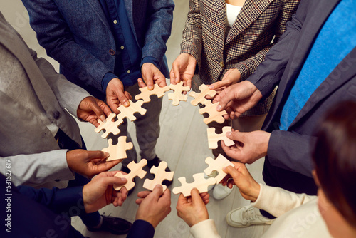Team of business people connecting jigsaw pieces. Group of multiracial men and women make a circle from different wooden jigsaw puzzle parts. Teamwork concept. Cropped shot. Conceptual background