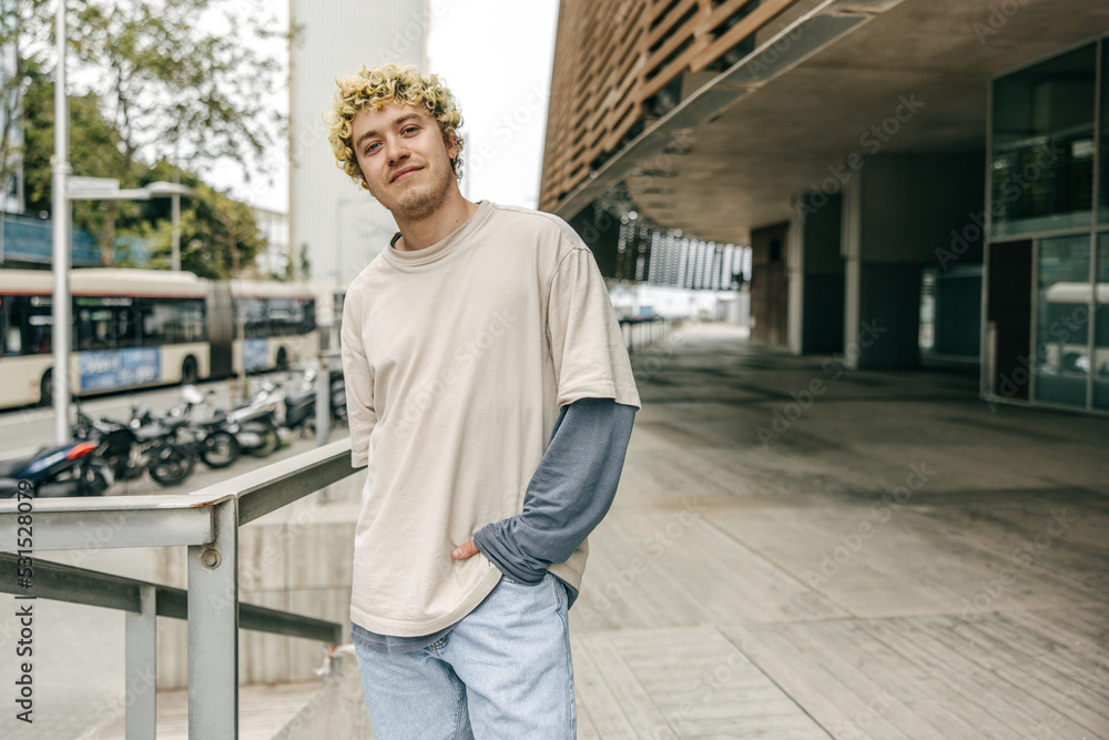 Stylish young caucasian man posing looking at camera at center of city. Curly blonde wear casual clothing holding hand in pocket. Concept lifestye. Stylish young caucasian man posing looking at camera at center of city. Curly blonde wear casual clothing holding hand in pocket. Concept lifestye.