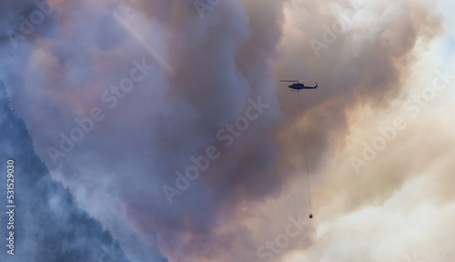 Wildfire Service Helicopter flying over BC Forest Fire and Smoke on the mountain near Hope during a hot sunny summer day. British Columbia, Canada. Natural Disaster