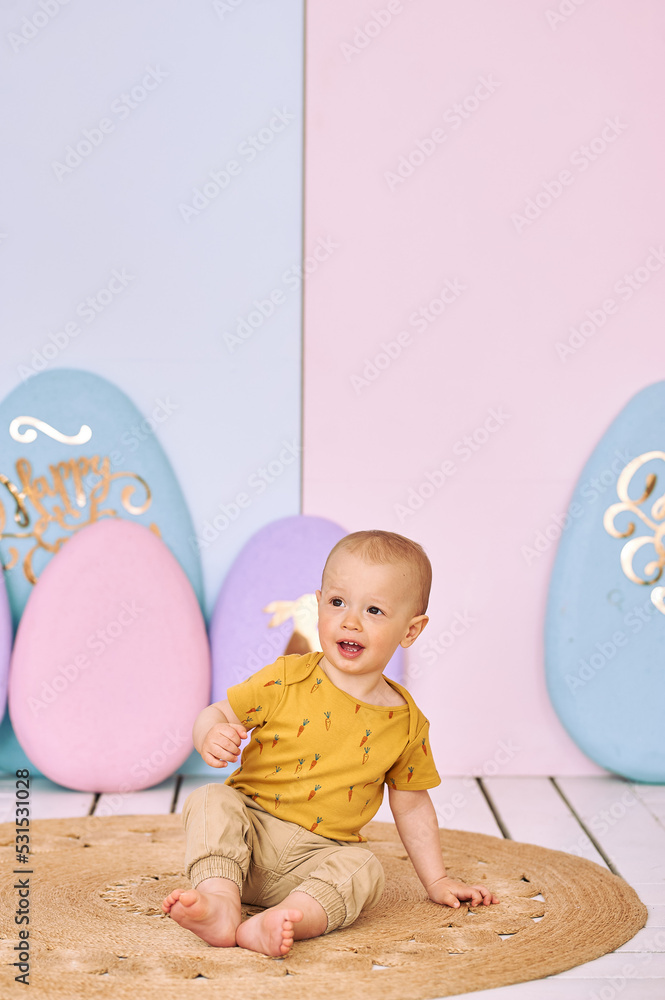 1 year old boy in yellow T-shirt, Easter decor, boy near two bunnies and large eggs