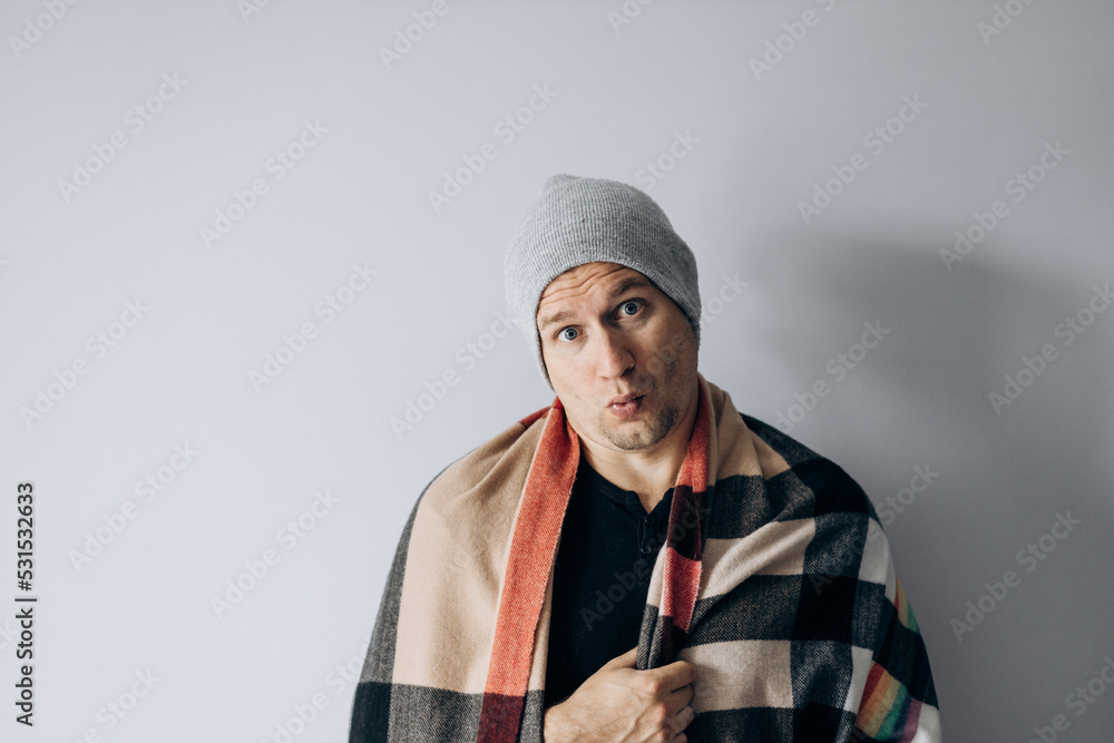 Guy is wrapped in blanket and warms his hands from the cold. Heating season. Winter has come, turned off heating. Guy is wrapped in blanket and warms his hands from the cold. Heating season. Winter has come, turned off heating.