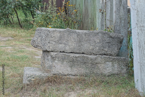 three old gray concrete blocks lie in the grass on the street near the fence