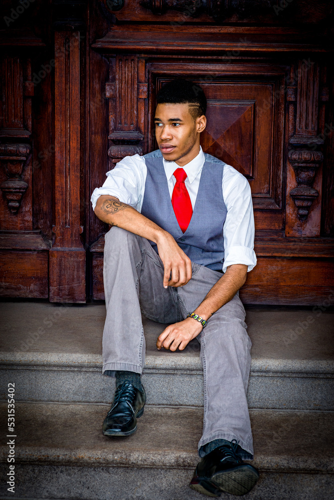 Young Man sitting on stairs by wooden office door in New York City, taking work break.