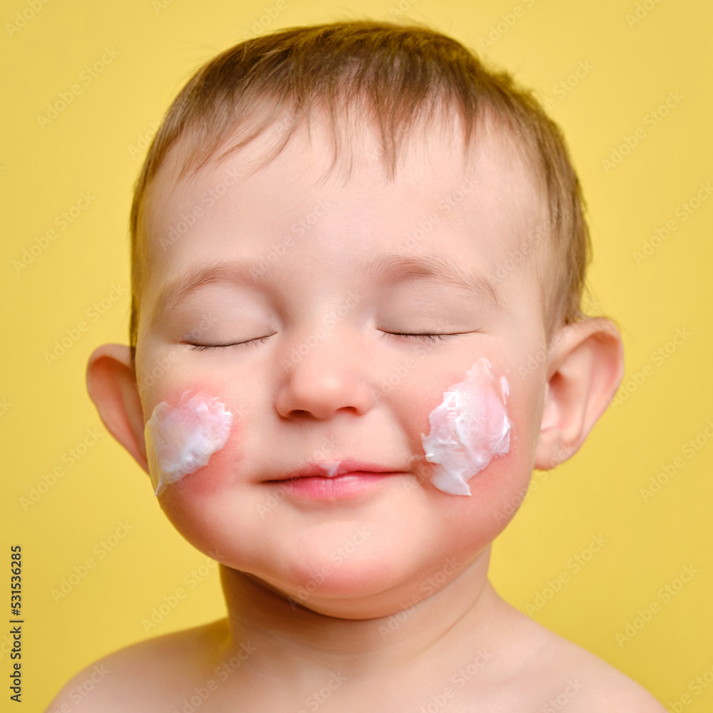 Face cream toddler baby, studio yellow background. Close-up portrait of a cute baby with cream on her cheeks. Kid aged one year and two months Face cream toddler baby, studio yellow background. Close-up portrait of a cute baby with cream on her cheeks. Kid aged one year and two months