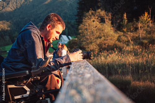 Young photographer with disability taking a photo of mountain nature at dusk, enjoying stunning view, handheld shot.