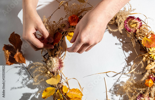 Women's hands creates an autumn wreath from natural materials on a white background.