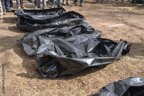 Several empty corpse body bag lie on the ground. People gathered around.