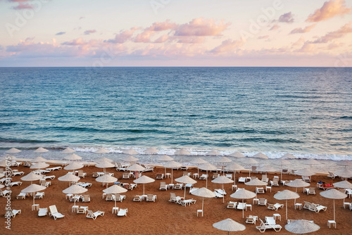 Sun loungers on the sandy beach, sea and clouds at sunset