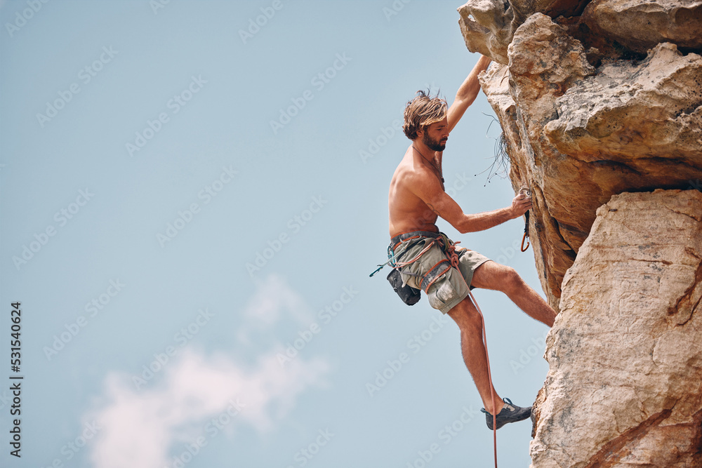 Man mountain or rock climbing while cliff hanging and adrenaline athlete on  adventure and check safety equipment, hook and rope. Fearless man doing  fitness, exercise and workout during extreme sport Stock Photo