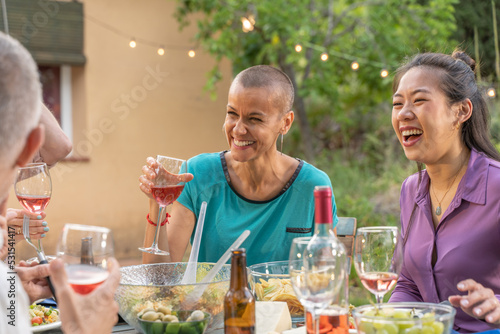 Multiracial friends eating and drinking happy smiling and laughing in the patio. Middle-aged cheerful people around the table.