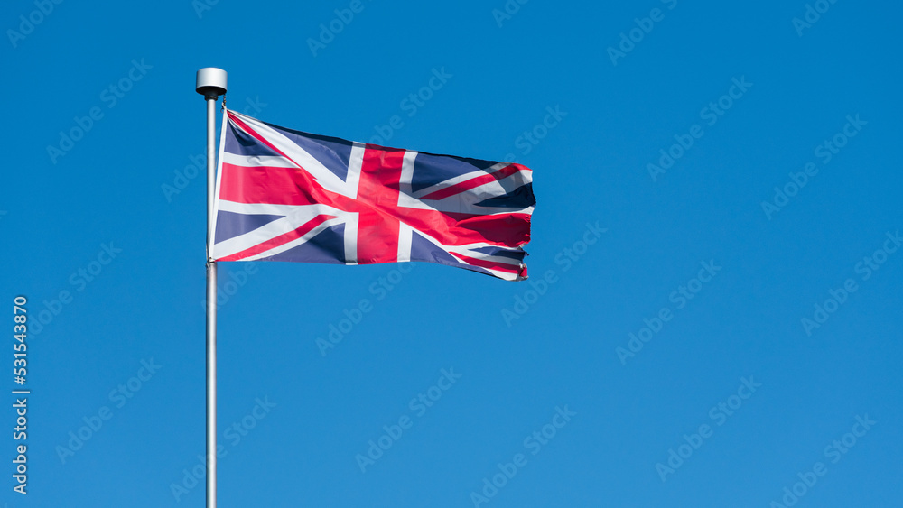 English flag Union Jack waving in the wind. UK flagpole and blue sky background