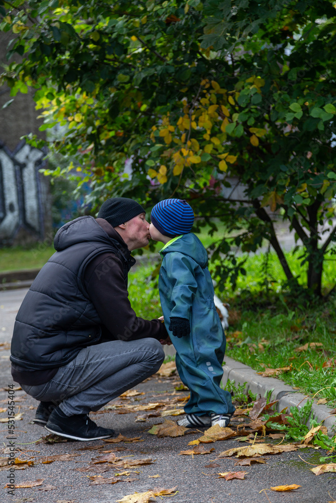 father and little son in the fall on a walk studying the leaves in the park on the street in the yard father and little son in the fall on a walk studying the leaves in the park on the street in the yard
