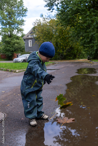 A boy of two years old throws autumn maple leaves into a puddle on the street
