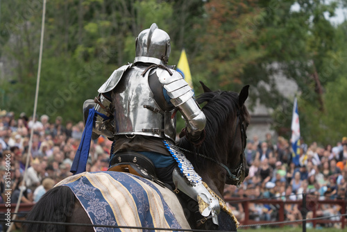 unknown knight in a suit of armor is riding on a horse and ready for battle