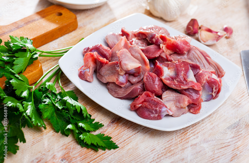 Fresh chicken gizzards on plate on wooden background with parsley, garlic and onion