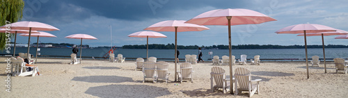 Canvas Print Web banner of pink beach umbrellas and Adirondack chairs at the sunny lakeshore