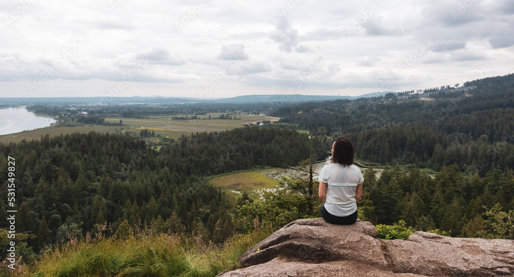 Adventurous Woman Standing on top of a rock overlooking the Canadian Nature Landscape.