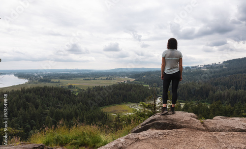 Adventurous Woman Standing on top of a rock overlooking the Canadian Nature Landscape.