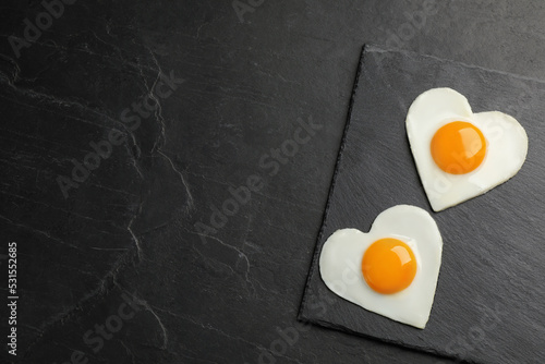 Heart shaped fried eggs on black table, top view. Space for text