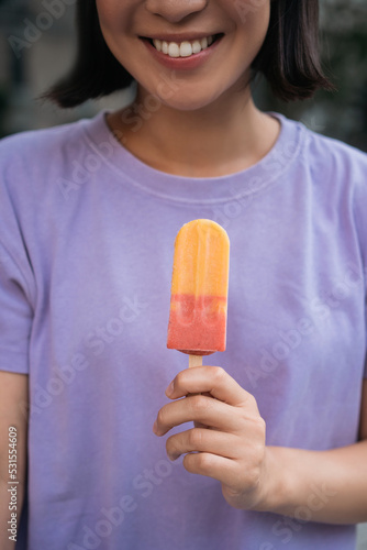 Cropped image of smiling asian woman wearing purple t shirt holding ice cream  