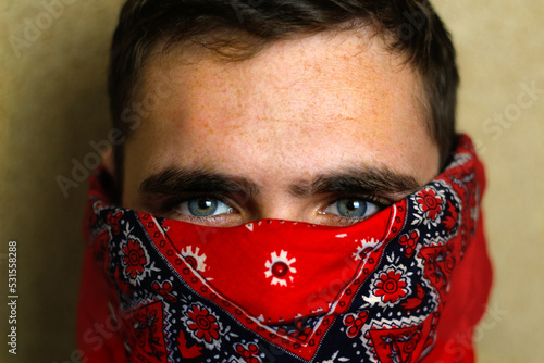 Defocus young man in red bandana. Closeup blue dark eyes. Man with his face hidden behind a bandanna stares balefully at the camera. Out of focus photo