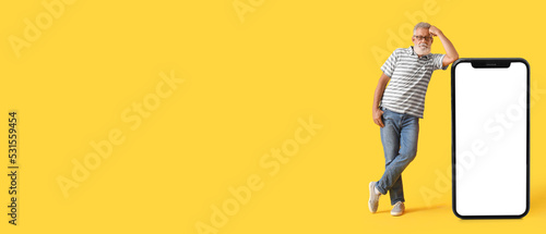 Mature man and big smartphone on yellow background with space for text