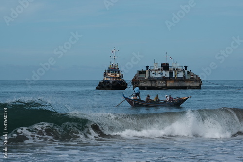 A small fishing boat surrounds two boats where fish are stored amid the violent waves that stand still in the sea