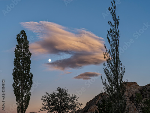 The moon rises behind a translucent wave cloud (altocumulus lenticularis) at dusk near Teasdale, Utah, USA photo