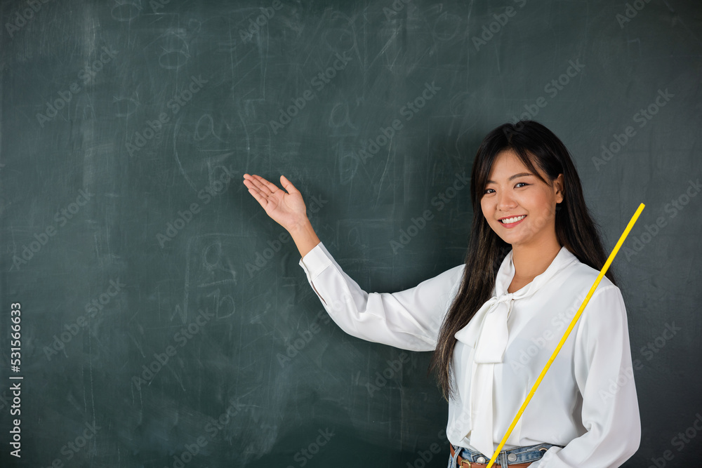 Back to school concept. Happy beautiful young woman standing hold pointer to back board, Asian female teacher smiling with wooden stick pointing to blackboard at school in classroom, Education Back to school concept. Happy beautiful young woman standing hold pointer to back board, Asian female teacher smiling with wooden stick pointing to blackboard at school in classroom, Education