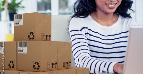 Caucasian woman using laptop shopping online with a pile of boxes 