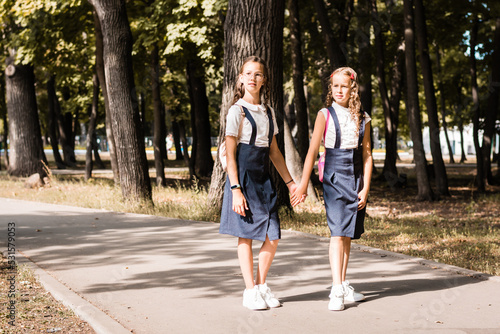Two elementary school girls smile and hold hands and go to school on a warm day