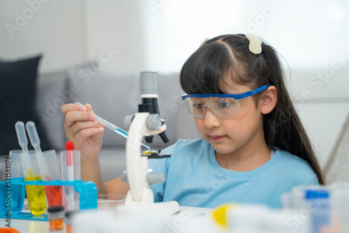 Portrait of little scientist in protective glasses playing with microscope in living room