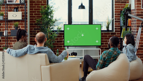 Group of people enjoying movie on television with greenscreen template, having fun at gathering. Watching cinema tv film with isolated chroma key background and blank mockup at home.